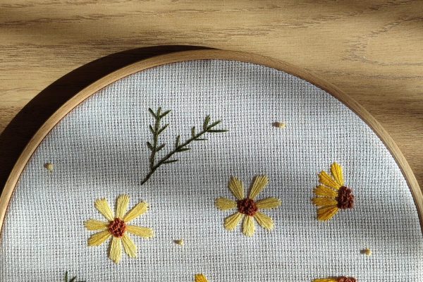 Broderie de fleurs jaunes sur une toile tendue dans un tambour en bois